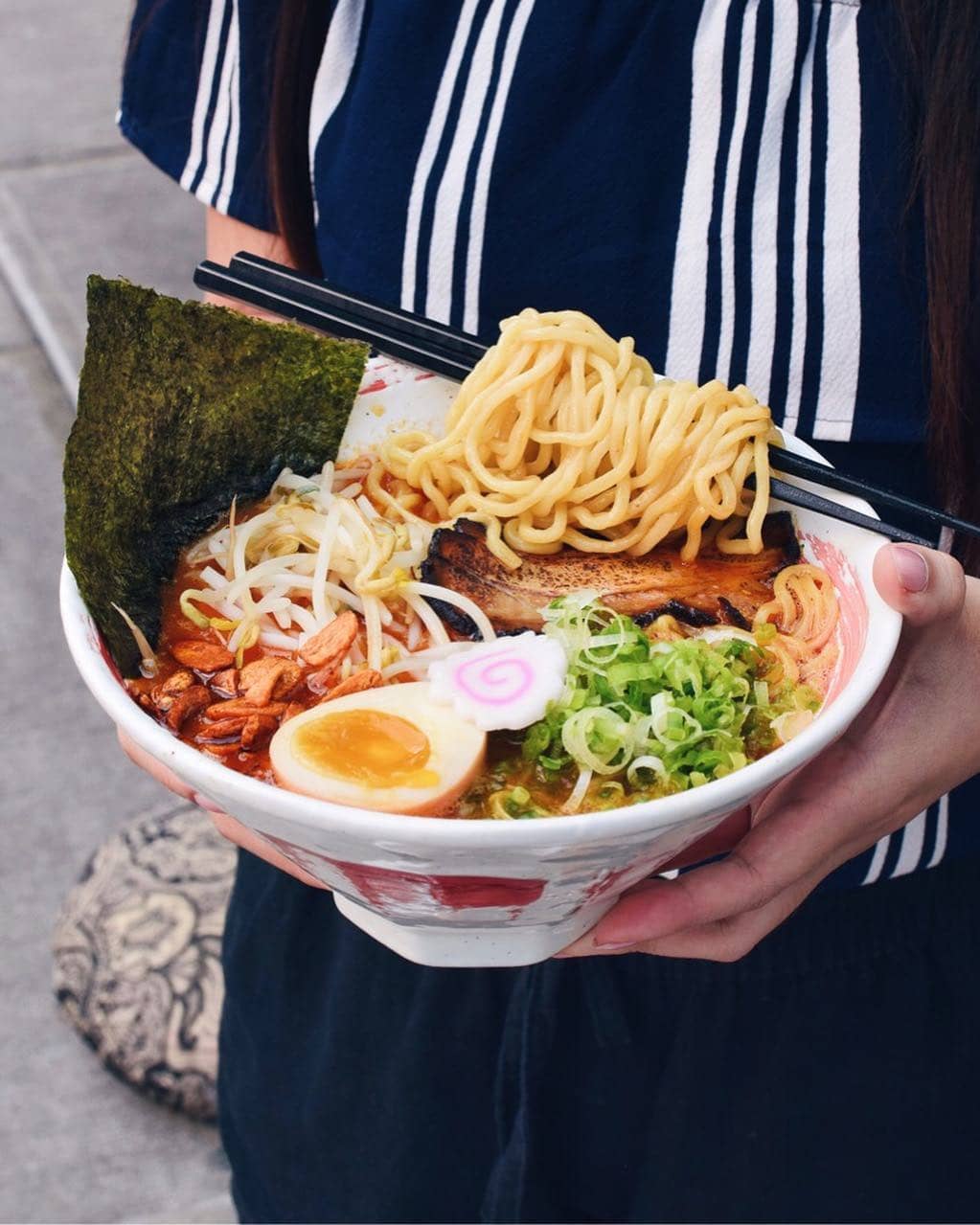 holding ramen bowl with noodles, eggs, bean sprouts