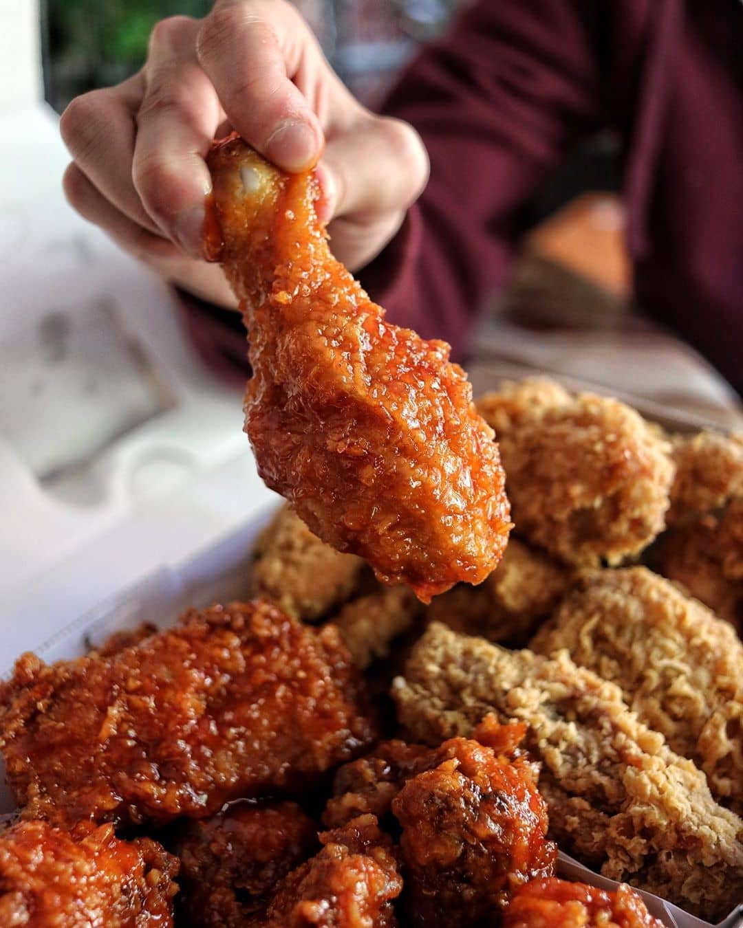 red fried chicken drumstick held above a pile of fried chicken