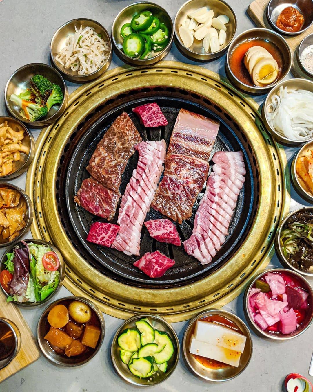 korean bbq meat on grill and small bowls banchan surrounding bbq