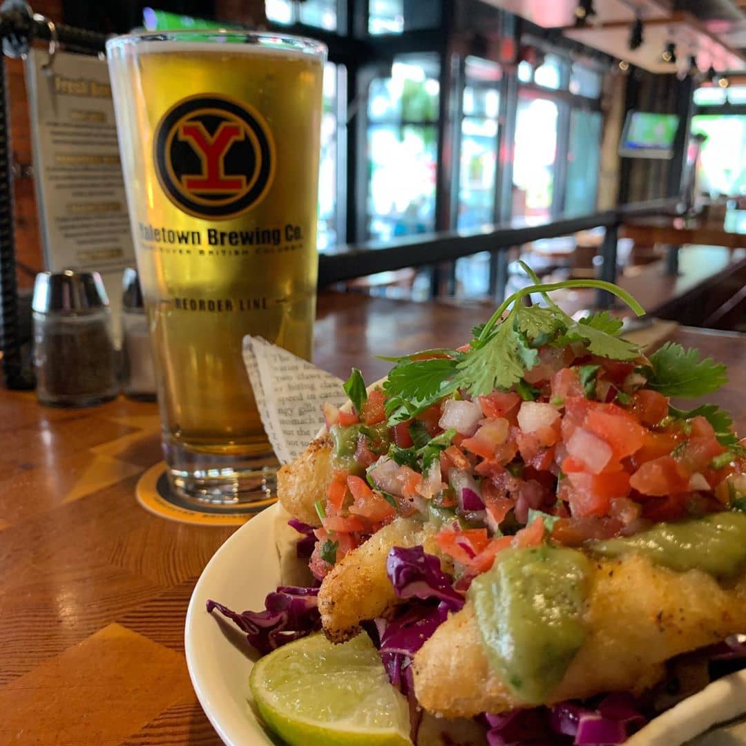 fish taco with salsa and pint of lager on table