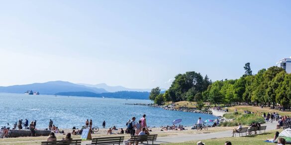 best beaches in vancouver - english bay west end with people sitting on grass and logs