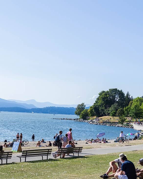best beaches in vancouver - english bay west end with people sitting on grass and logs