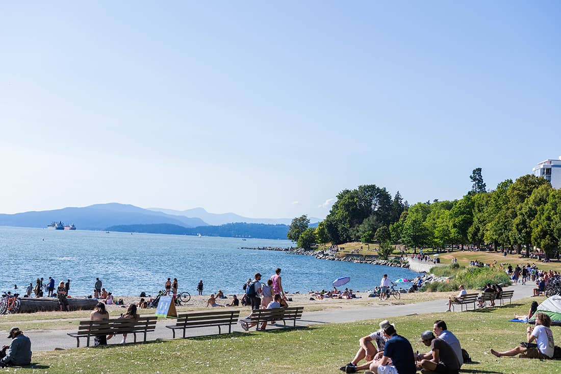 best beaches in vancouver - english bay west end with people sitting on grass and logs