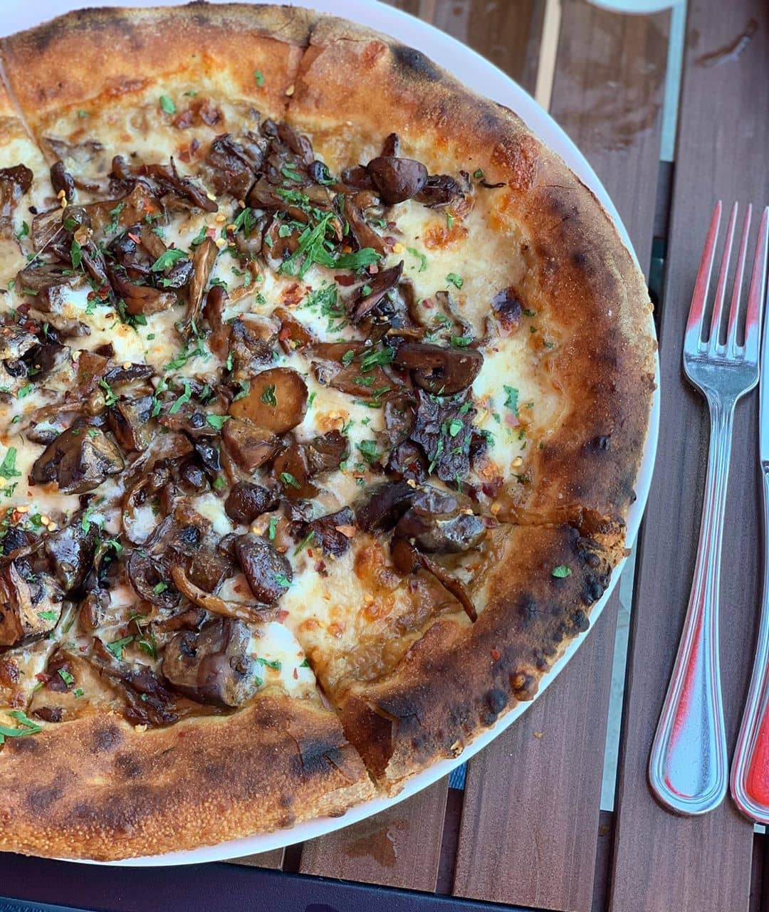 mushroom pizza on wooden table with fork beside