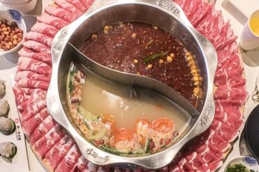 Hot pot in middle with two soup bases and ring of meat surrounding it