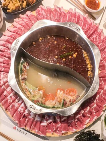 Hot pot in middle with two soup bases and ring of meat surrounding it