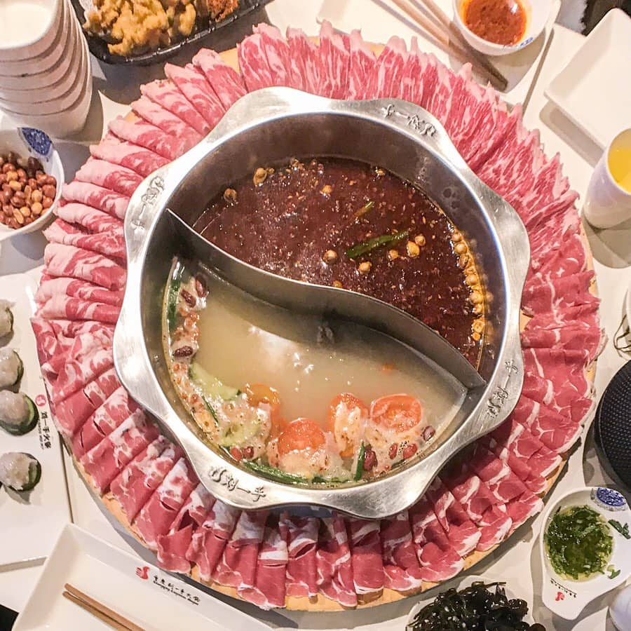 Hot pot in middle with two soup bases and ring of meat surrounding it