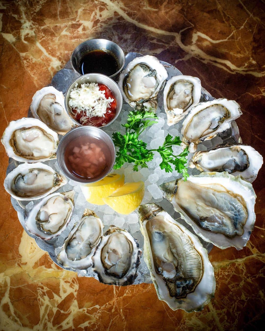 A close-up photo of a plate of fresh oysters on the half shell with lemon wedges and mignonette sauce on crushed ice. The plate is from Joe Fortes Seafood & Chop House in Vancouver, Canada. (Photo Credit: Joe Fortes Seafood & Chop House via Noms Magazine Ltd.)