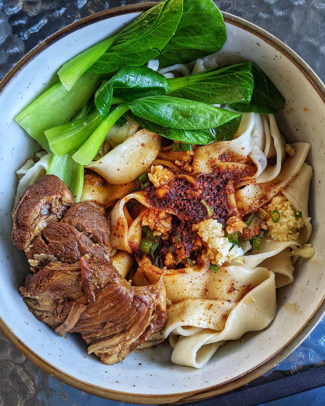 bowl of hand pulled noodles, leafy greens, and stewed pork on a glass table best west vancouver restaurants - lao cai chinese cuisine