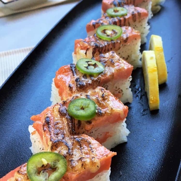 salmon aburi on long black plate with two lemon slices on table best west vancouver restaurants - raku japanese kitchen